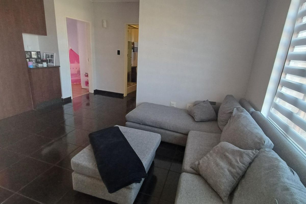 A living room area featuring dark tiled flooring and modern venetian blinds, providing access to adjacent rooms within the apartment.