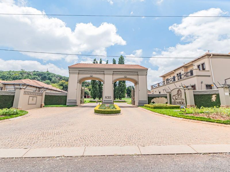 Grand gated entrance to Leeuwberg estate featuring a paved driveway, manicured landscaping, and secure perimeter walling with electric fencing.