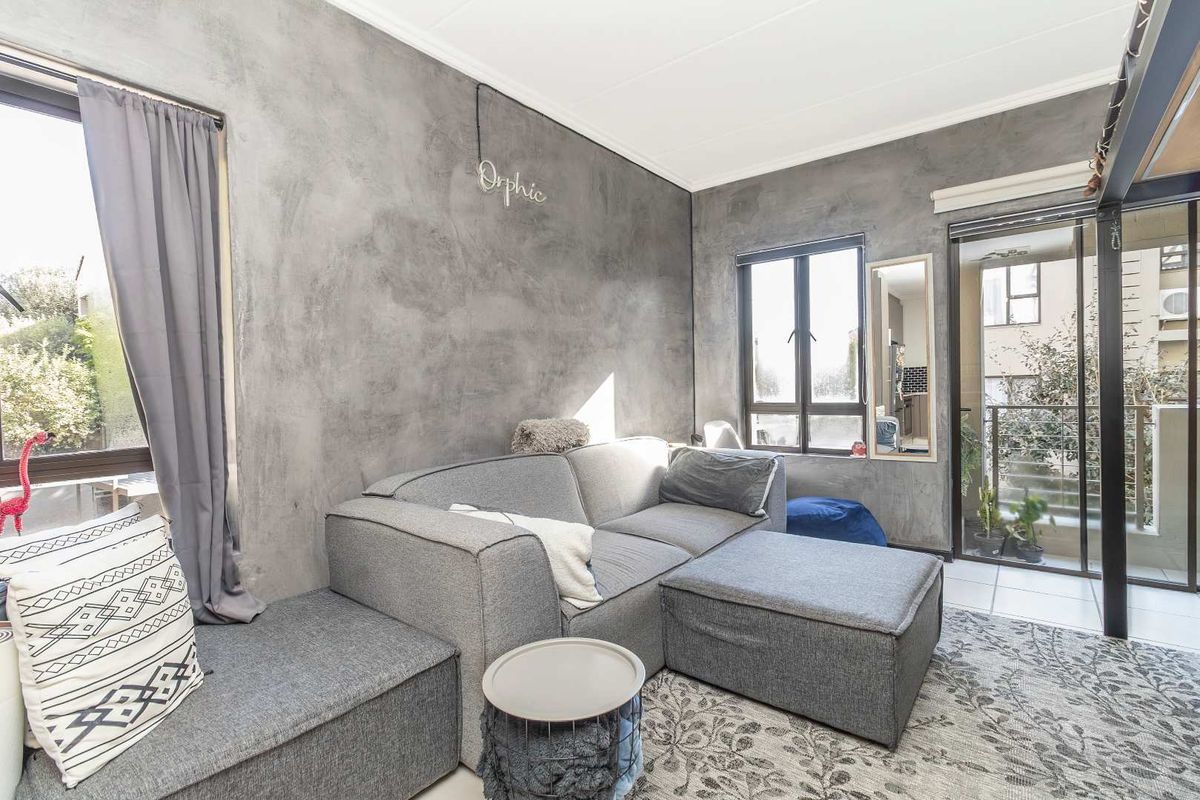 A modern living room featuring a textured cement-finish feature wall, tiled flooring, and a sliding glass door providing access to an outdoor balcony area.