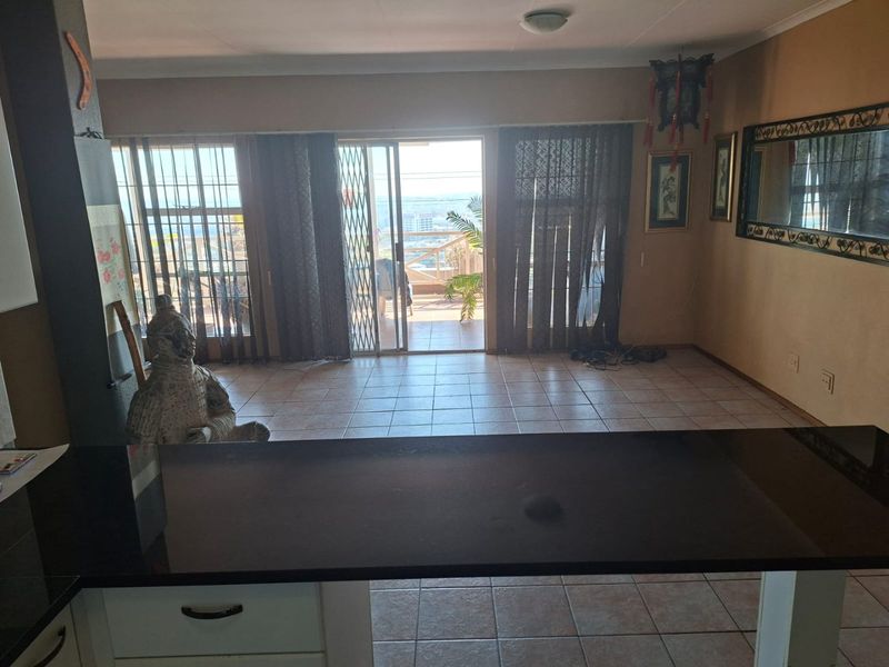 Open plan living area featuring tiled flooring, a breakfast bar, and sliding glass doors leading to an outdoor balcony with scenic views.