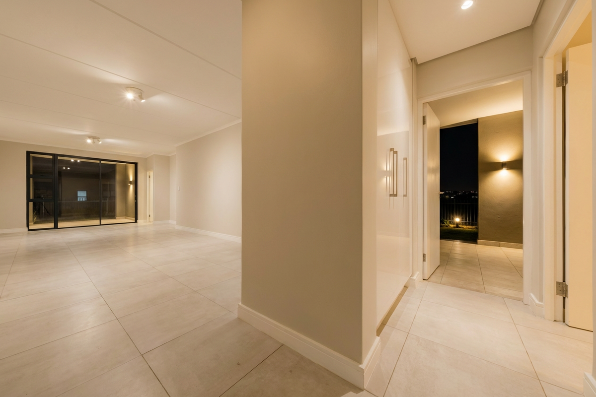 Spacious, modern open-plan living area featuring neutral tiled flooring, recessed lighting, and seamless access to an outdoor balcony through large sliding glass doors.