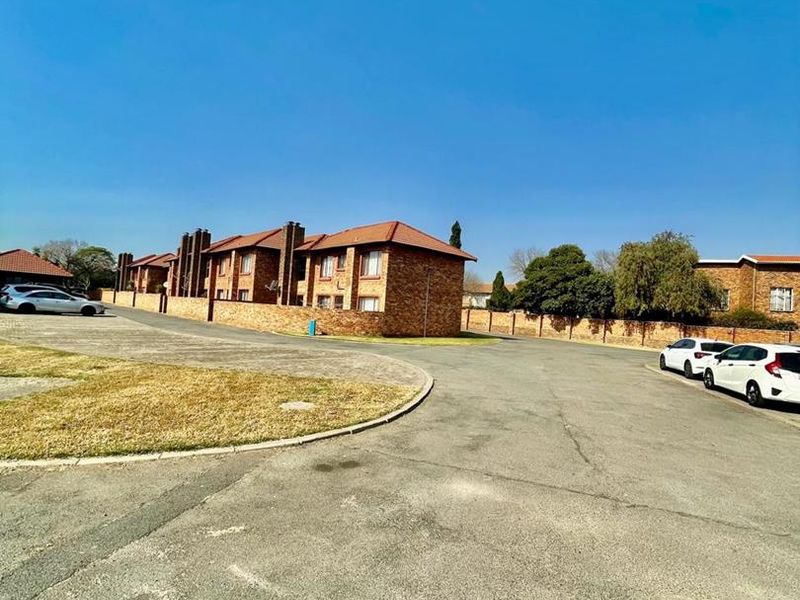 Exterior view of a face-brick cluster complex featuring a tiled roof and paved driveway access within a residential estate.