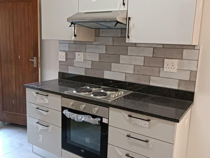 A modern, newly installed kitchen featuring sleek cabinetry, a granite countertop, built-in oven, electric hob, and a stylish tiled backsplash.
