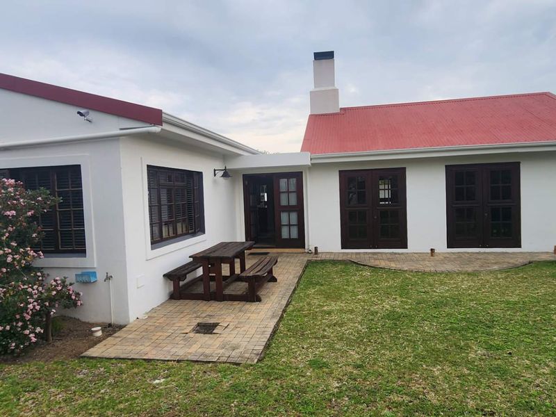 Rear view of the farmhouse featuring a red metal roof, brick paved patio area, and multiple timber-framed glass doors leading into the home.