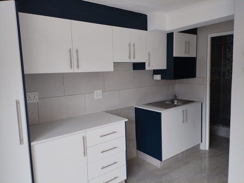 A modern, clean kitchen featuring white and navy cabinetry, stone countertops, a stainless steel sink, and a neutral tiled backsplash.
