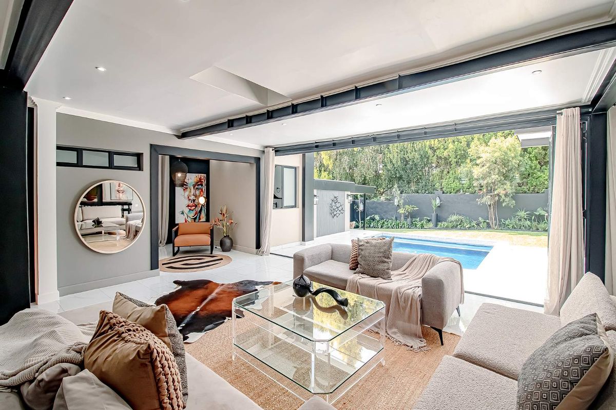 Modern open-plan living area featuring large stacking glass doors that seamlessly connect the interior space to the outdoor swimming pool and garden area.