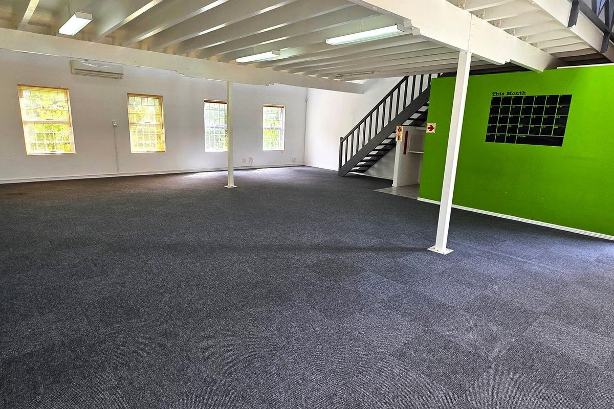 Spacious open-plan office area featuring carpeted flooring, exposed ceiling beams, and a staircase leading to an upper level.