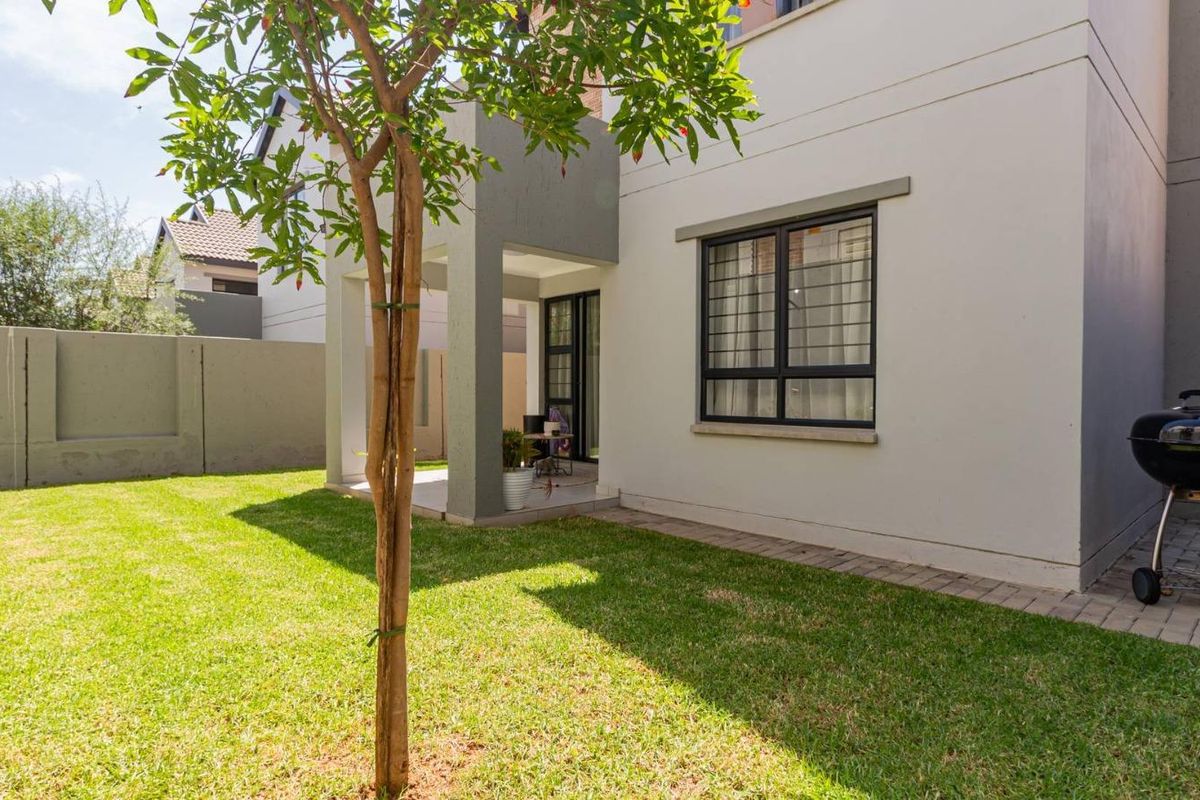 Rear view of the cluster property featuring a well-maintained lawn, a covered patio area, and secure aluminum-framed windows.