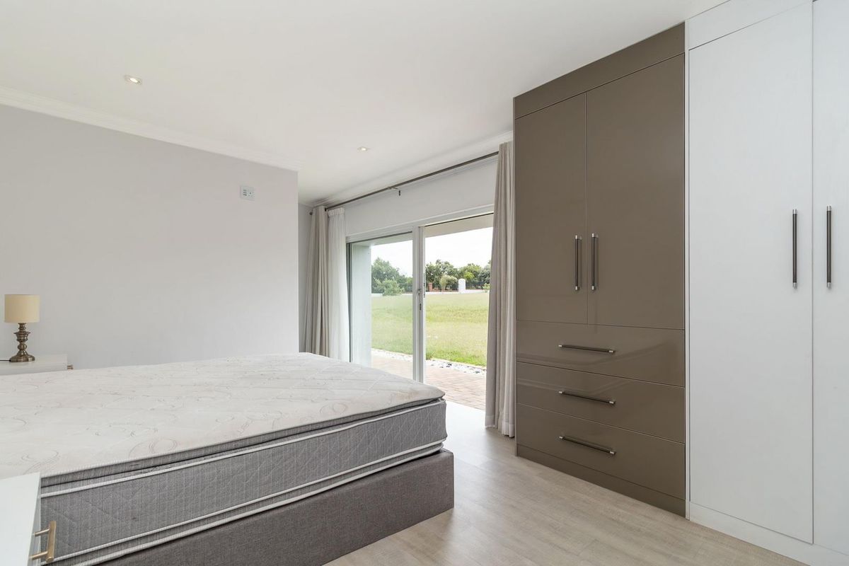 A bright bedroom featuring modern built-in cupboards, light wood-look flooring, and large sliding glass doors providing direct access to the garden.
