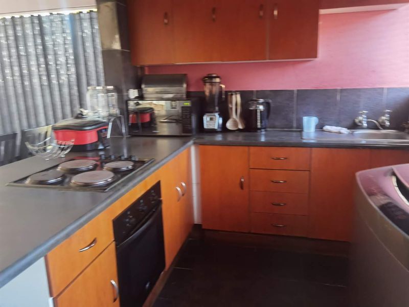 A functional kitchen featuring wooden cabinetry, dark laminate countertops, an integrated electric hob and oven, and a tiled backsplash.