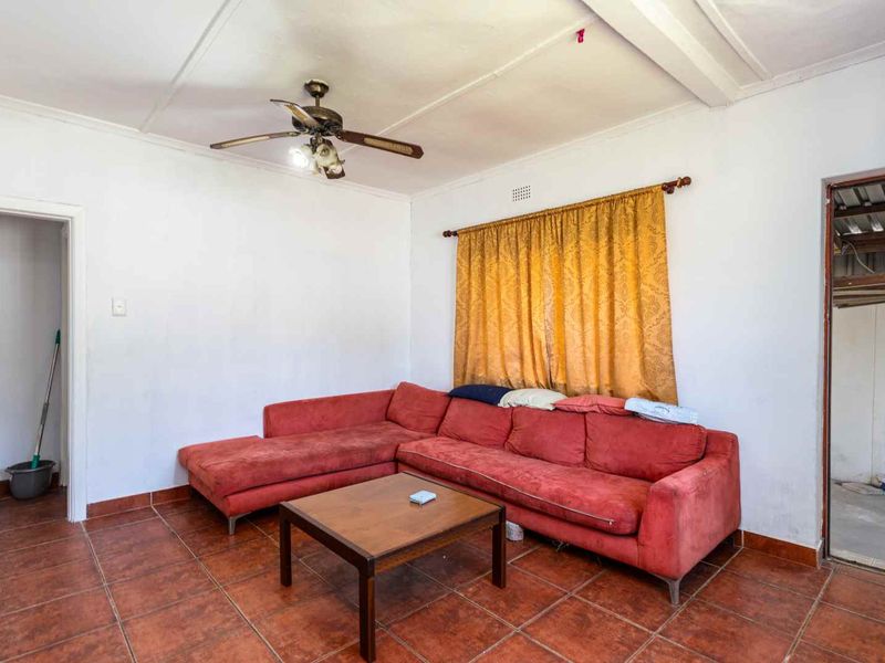 A living room featuring terracotta floor tiles, a ceiling fan, and neutral walls, offering a blank canvas for potential interior updates.