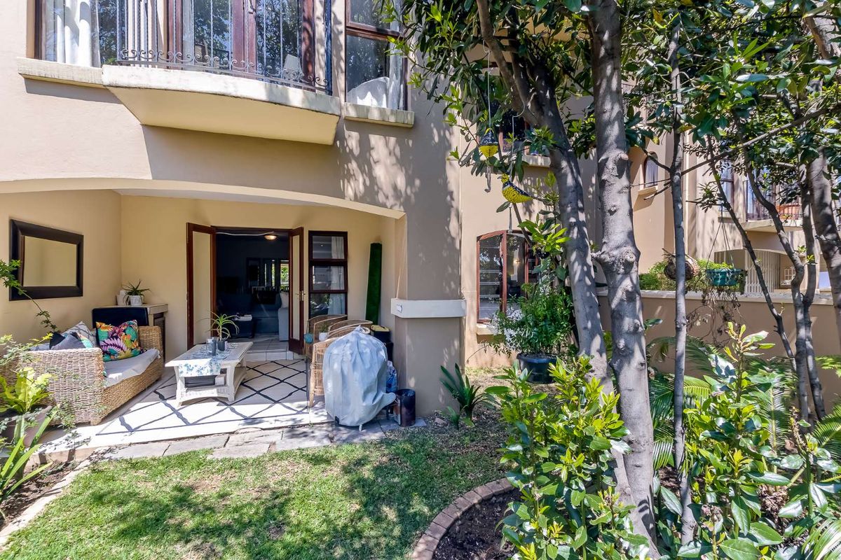 A rear view of the apartment featuring a covered patio area, landscaped garden, and access to the interior through double french doors.