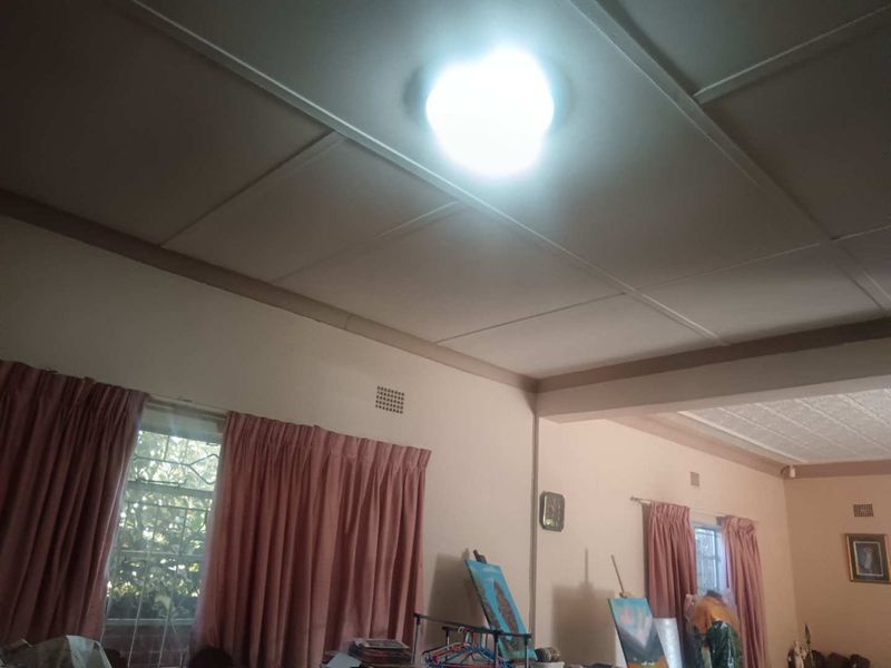 A living area featuring traditional ceiling panels, ventilation grilles, and windows fitted with security bars.