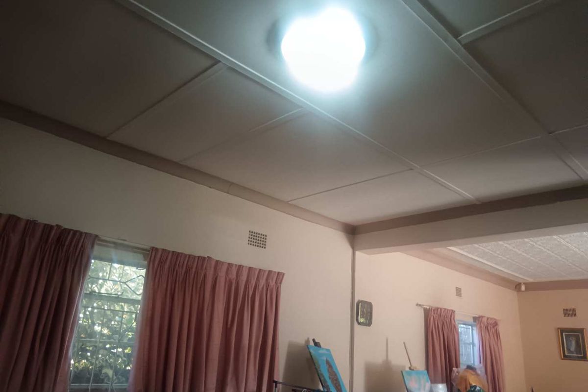 A living area featuring traditional ceiling panels, ventilation grilles, and windows fitted with security bars.