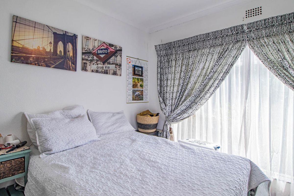 A cozy bedroom featuring a large window with curtains and a built-in ceiling ventilation unit.
