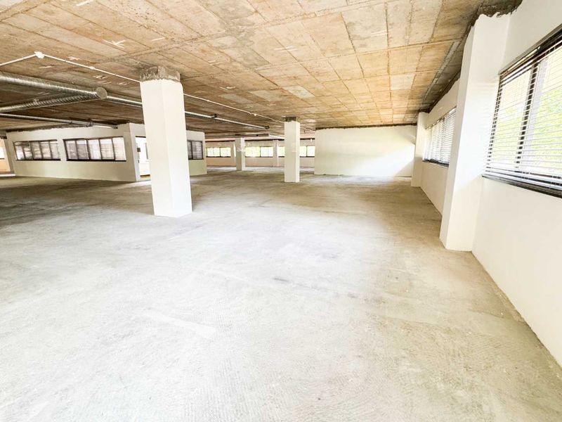 A large, open-plan commercial space featuring an exposed concrete ceiling, structural columns, and large windows with fitted blinds, currently in an unfinished shell condition.