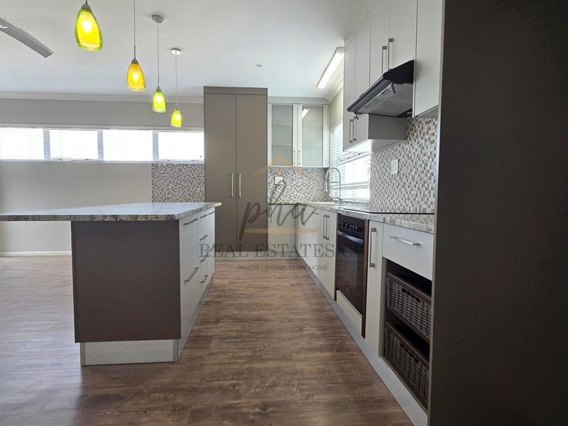 Modern kitchen featuring a central island, granite countertops, built-in oven, extractor fan, and stylish mosaic tile backsplash with wood-look laminate flooring.