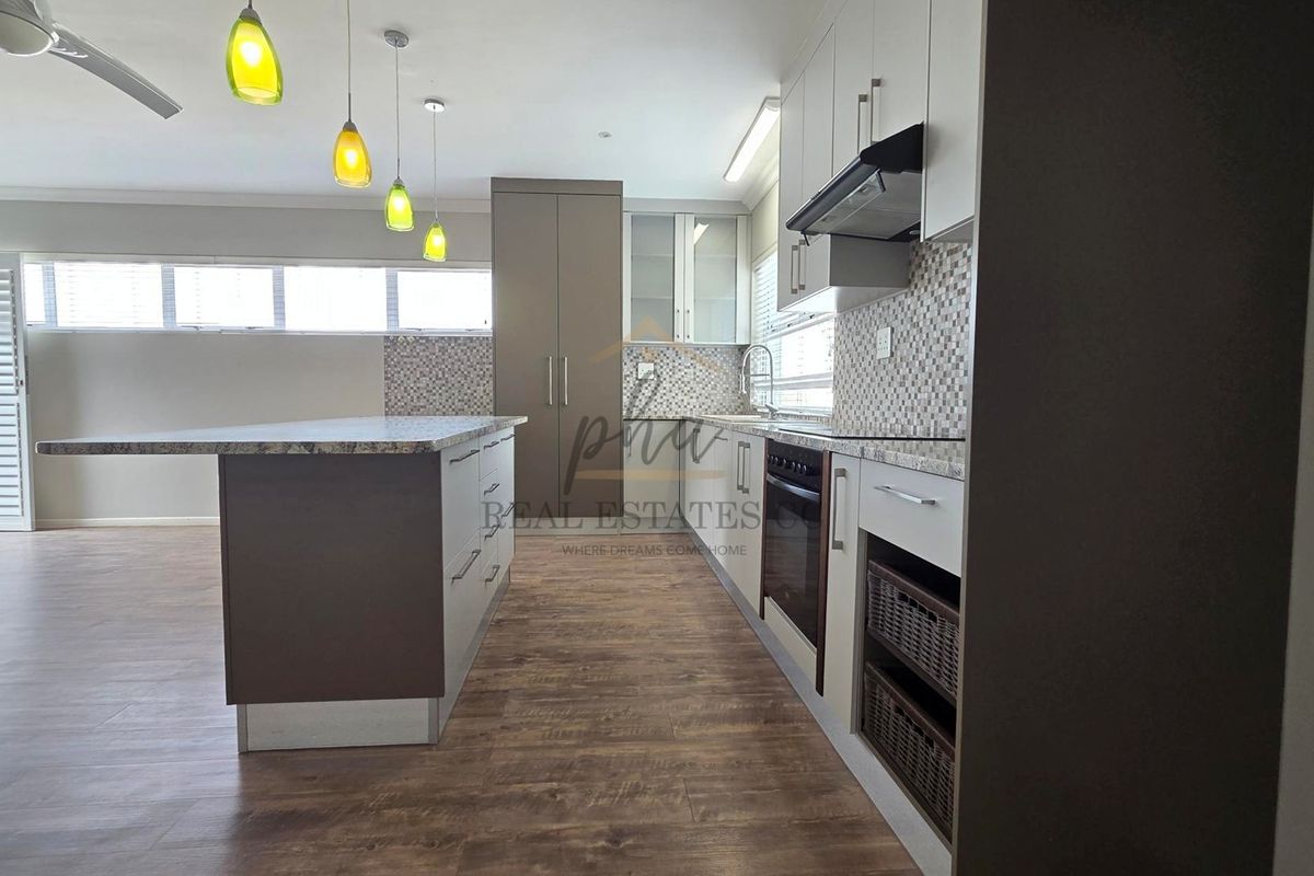 Modern kitchen featuring a central island, granite countertops, built-in oven, extractor fan, and stylish mosaic tile backsplash with wood-look laminate flooring.