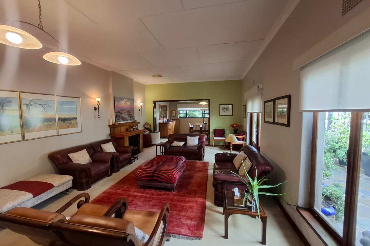 Spacious living room featuring a traditional fireplace, large windows with garden views, and an open-plan layout connecting to the adjacent dining area.