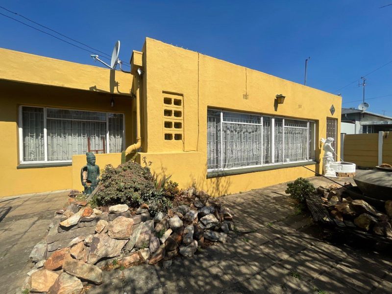 Rear exterior view of a yellow-painted house featuring a paved patio area, security window bars, and a satellite dish installation.