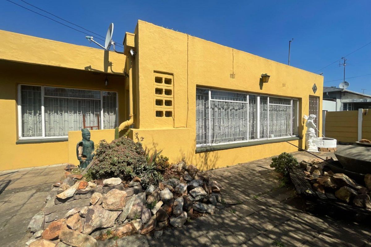 Rear exterior view of a yellow-painted house featuring a paved patio area, security window bars, and a satellite dish installation.