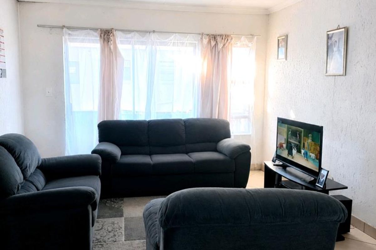 A functional living room featuring tiled flooring and natural light through a large window with curtain fittings.