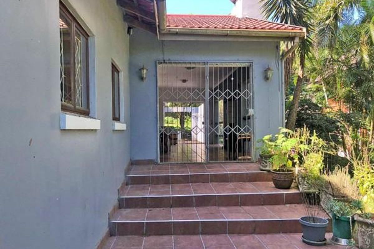 Rear exterior view featuring a tiled staircase leading to a covered patio area secured by a metal security gate.