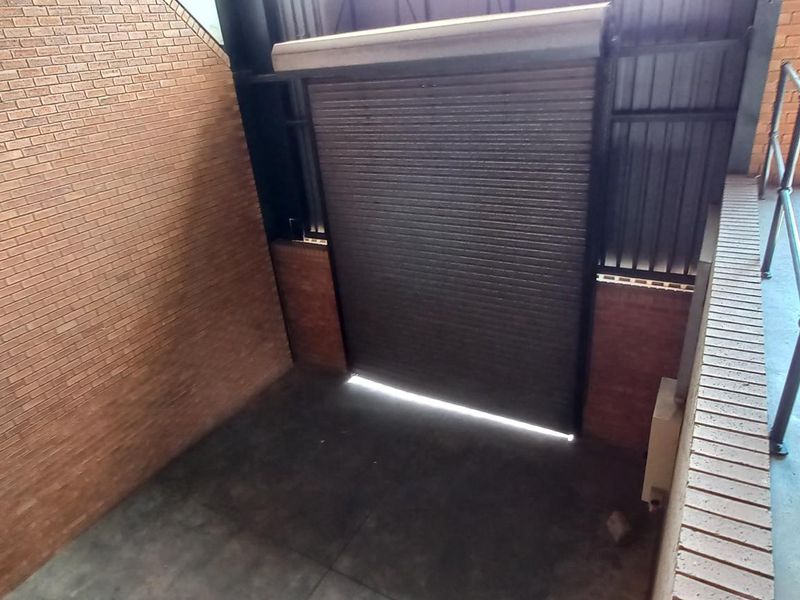 Industrial utility space featuring exposed brick walls, concrete flooring, and a secure roller shutter door with metal safety railing.