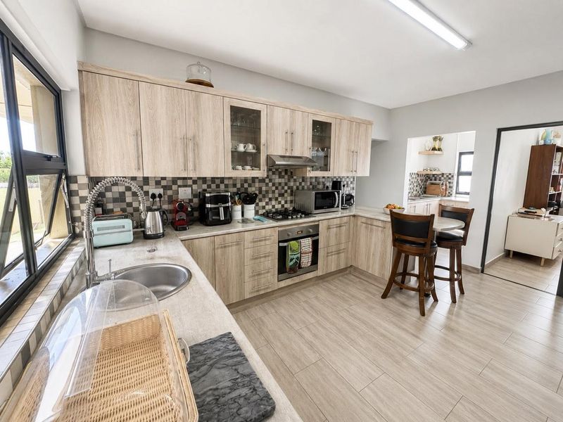 A functional kitchen featuring light wood-finish cabinetry, tiled backsplash, built-in oven with gas hob, and a stainless steel sink with a gooseneck faucet.