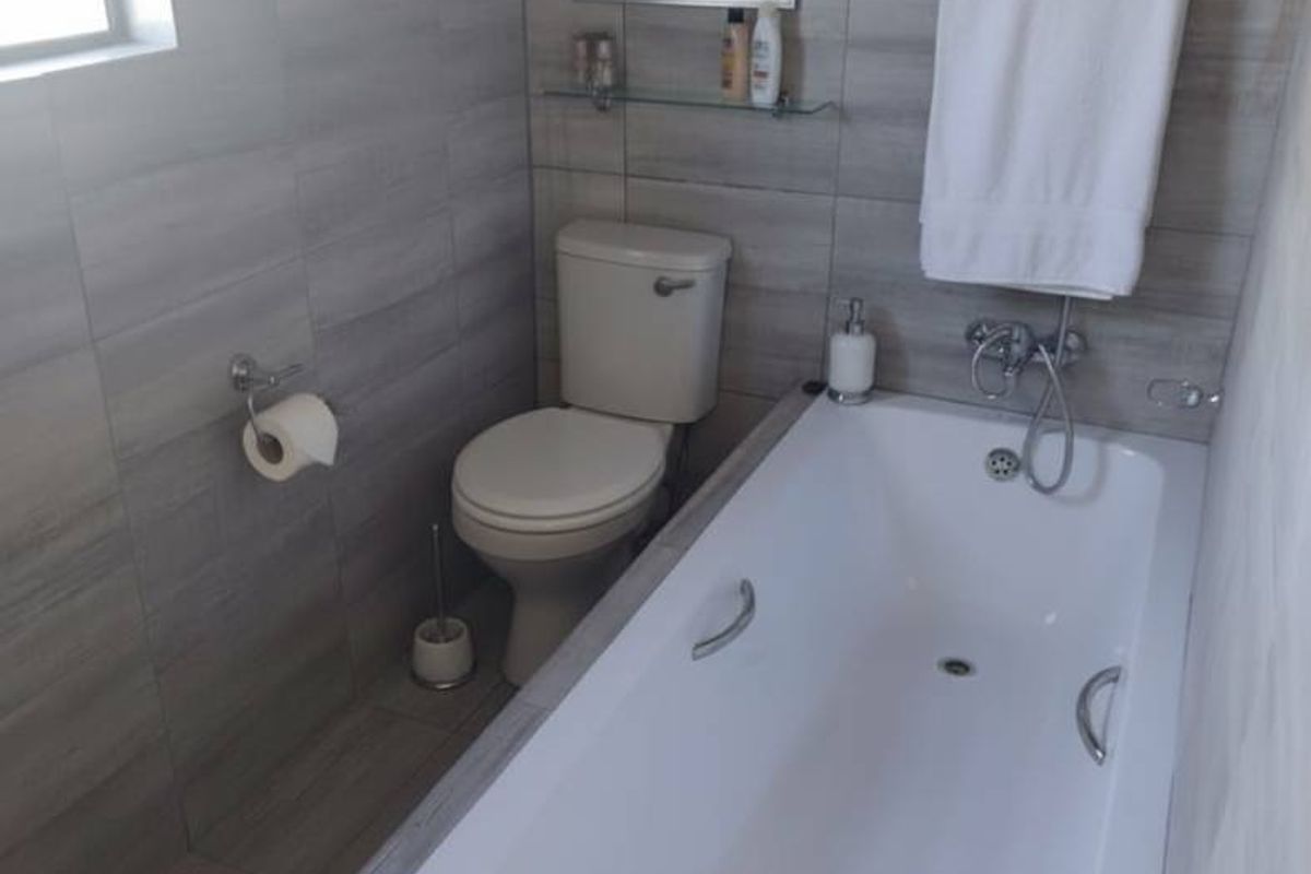 A modern bathroom featuring a built-in bathtub, a wall-mounted toilet, and neutral grey wall and floor tiling.