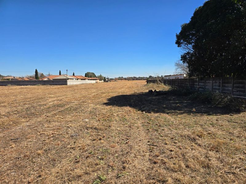 A view of a vacant residential plot featuring dry grass and established boundary wall fencing.