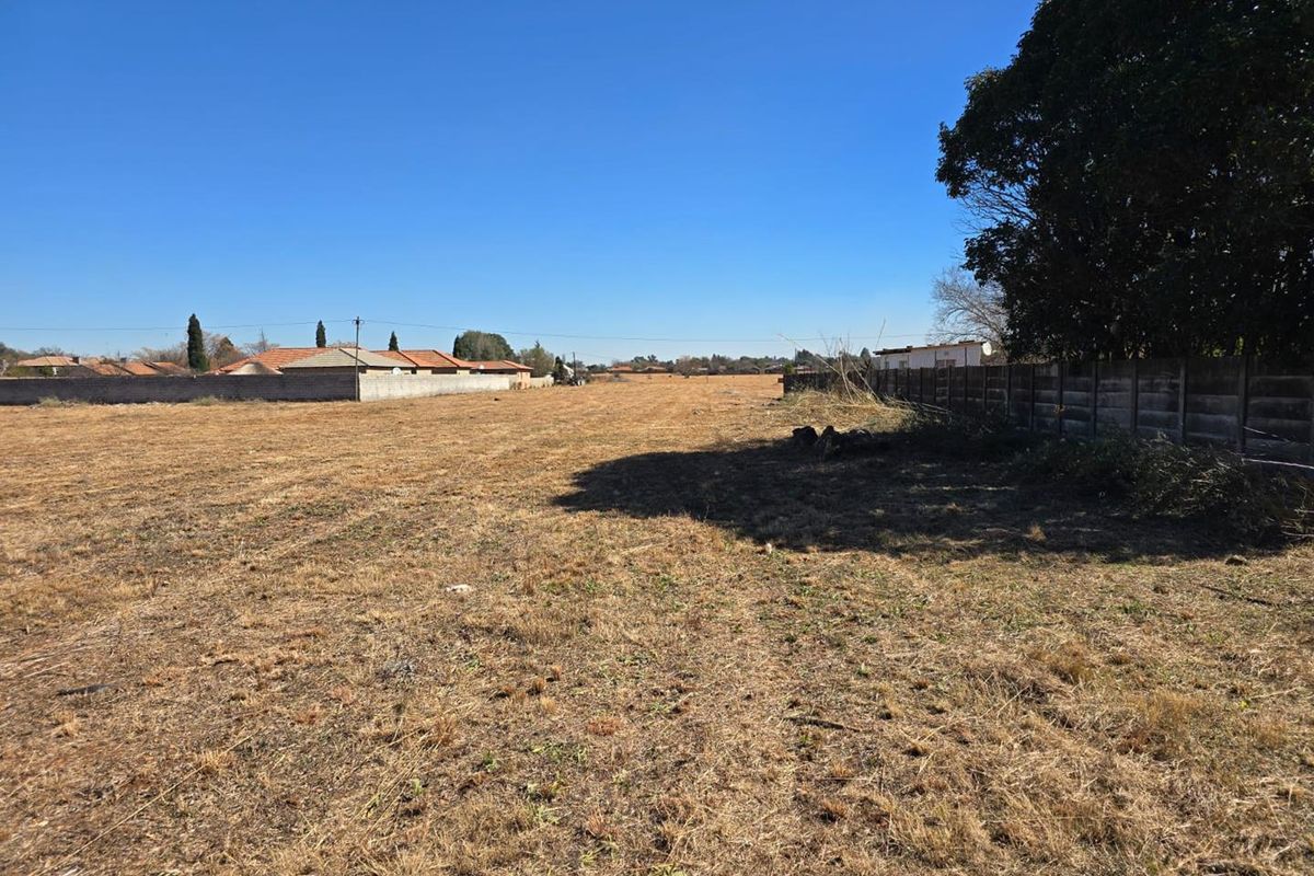 A view of a vacant residential plot featuring dry grass and established boundary wall fencing.