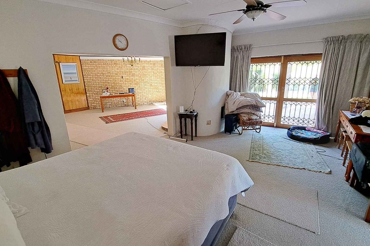 Spacious bedroom featuring a ceiling fan, built-in fireplace structure, and sliding glass doors leading to an outdoor area, with an adjoining living space.