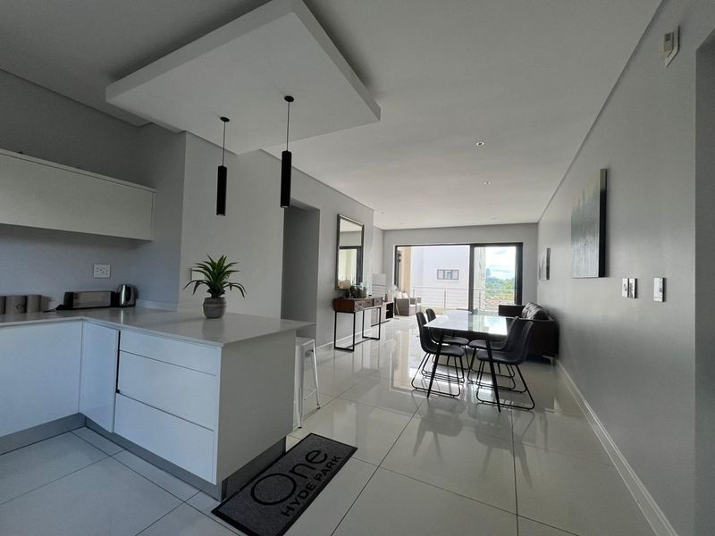 Modern open-plan living area featuring a sleek kitchen with stone countertops, recessed ceiling lighting, and large sliding doors leading to a balcony.