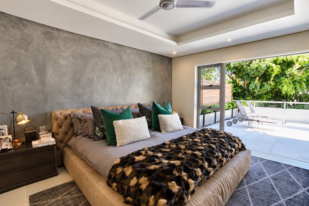 Spacious bedroom featuring a textured feature wall, recessed ceiling with fan, and large sliding glass doors opening onto a private balcony.