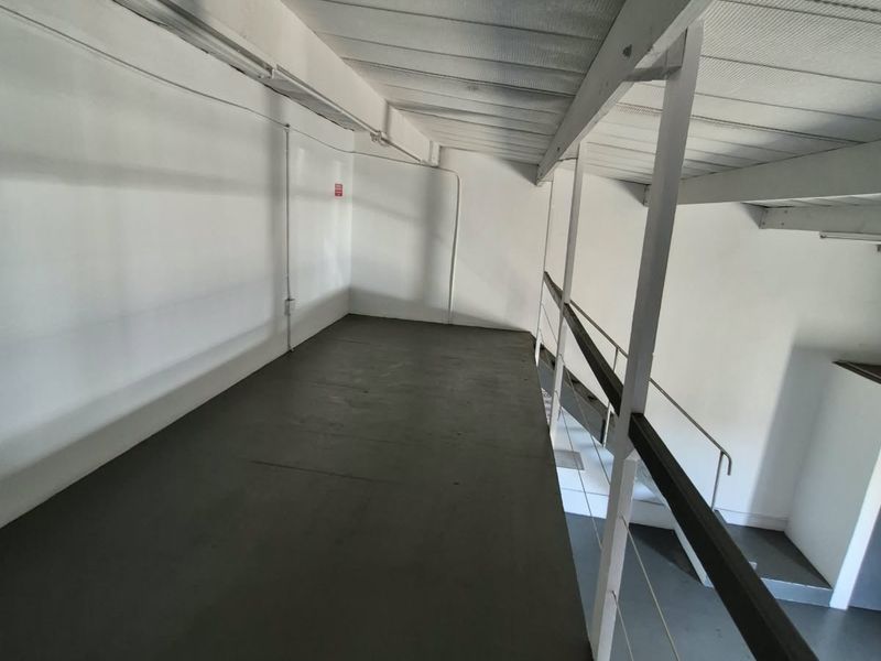 An open-plan mezzanine level featuring exposed structural steel beams, a metal staircase, and safety railings, suitable for storage or additional workspace.
