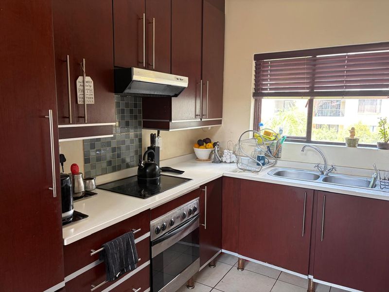 A functional kitchen featuring dark wood cabinetry, a built-in oven with electric hob, extractor fan, and a double sink with window views.