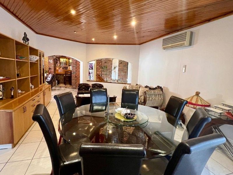 Spacious dining area featuring a distinctive timber-clad vaulted ceiling, tiled flooring, built-in cabinetry, and an open-plan layout with a brick archway.