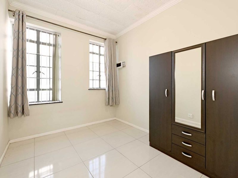 A bedroom featuring tiled flooring, security bars on the windows, and a built-in wardrobe with a central mirror.