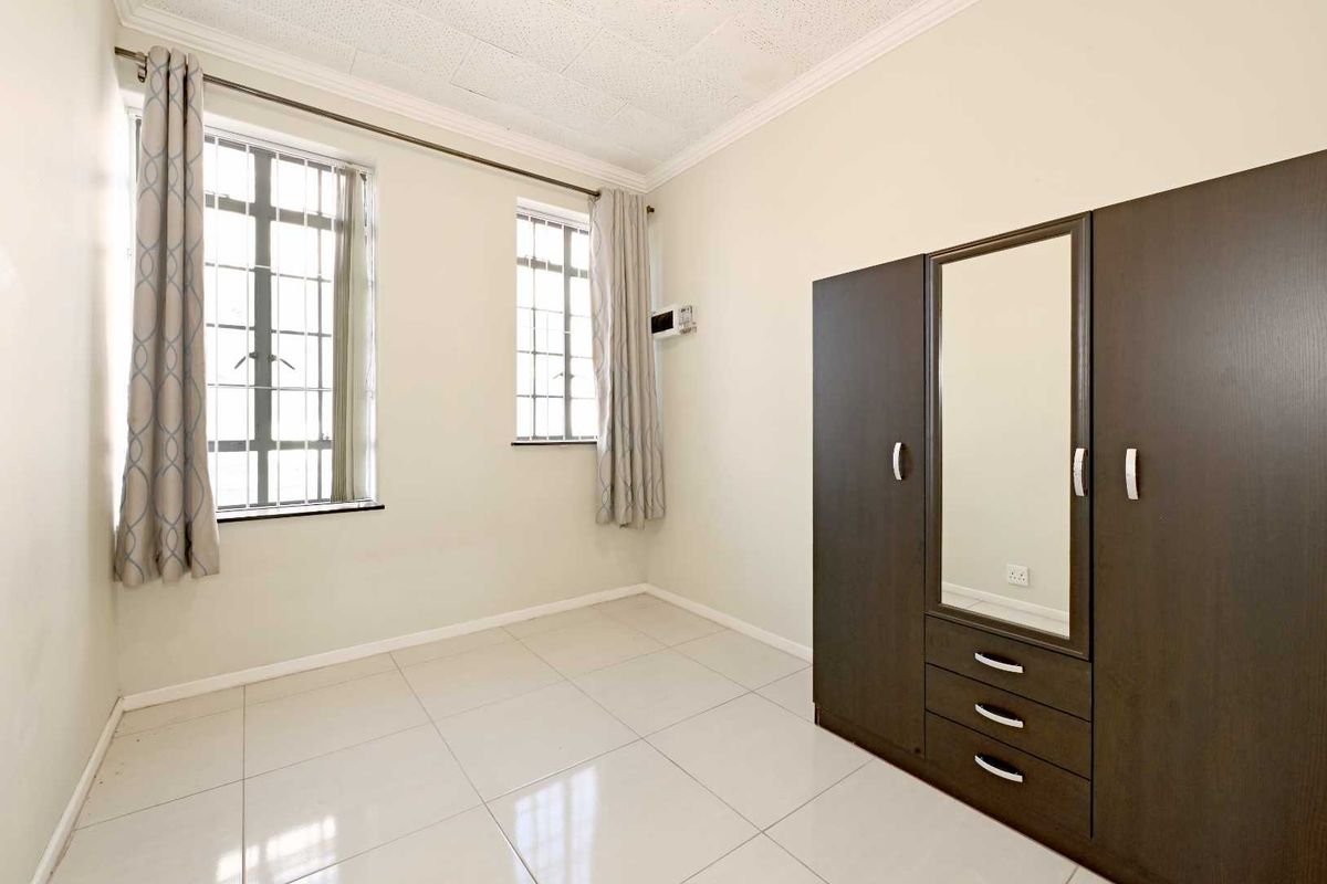 A bedroom featuring tiled flooring, security bars on the windows, and a built-in wardrobe with a central mirror.