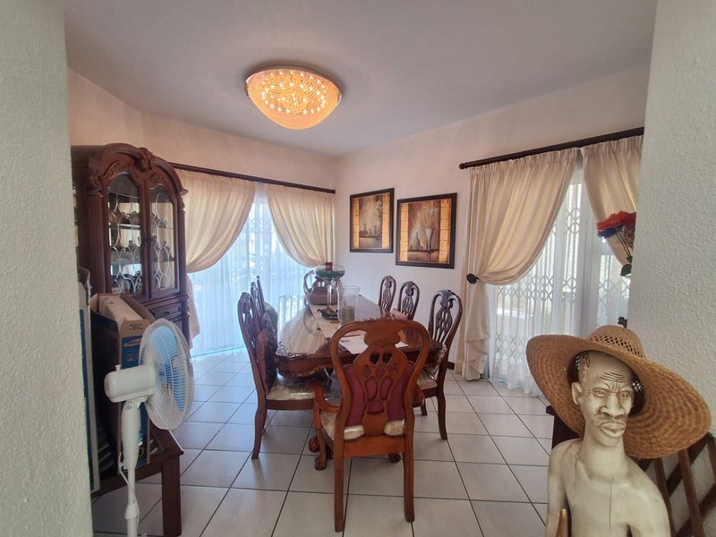 A dining room featuring tiled flooring, a central ceiling light fixture, and sliding glass doors with security gates providing access to the exterior.