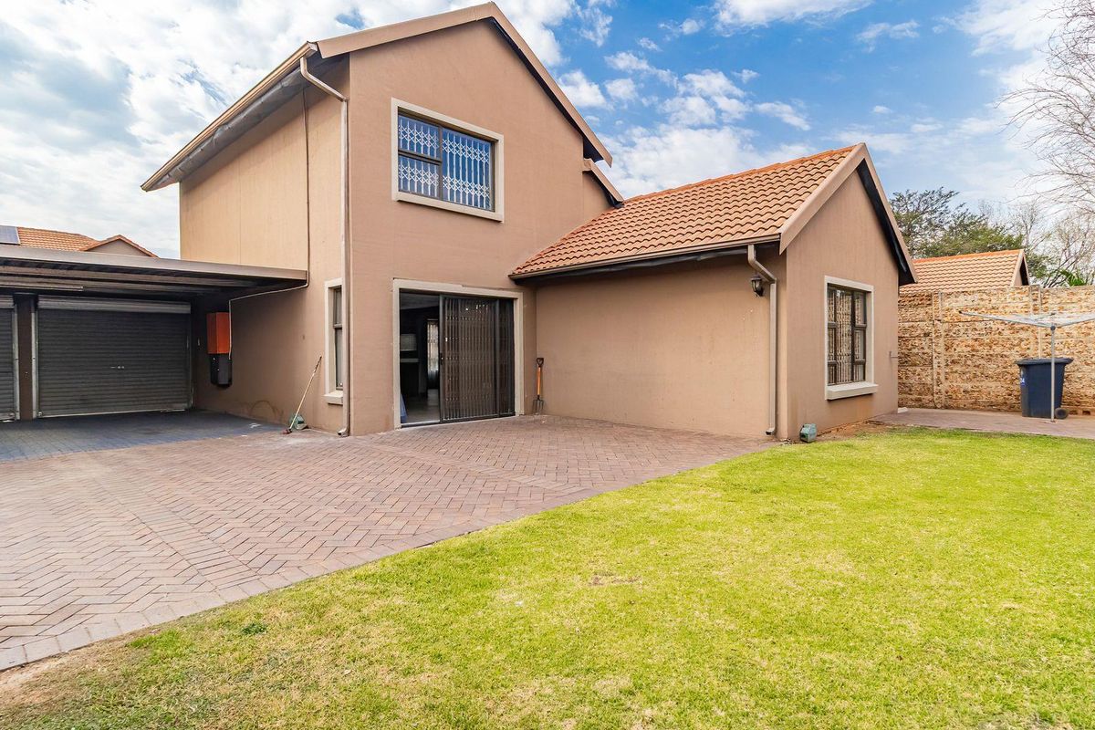 Rear view of the townhouse featuring a paved driveway, double garage, and a well-maintained lawn area.