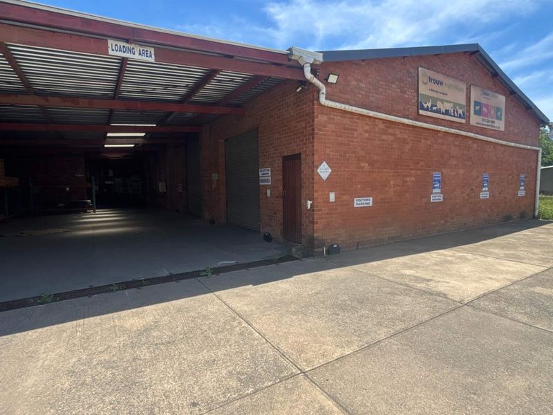 Industrial property exterior featuring a covered loading bay, brick facade, roller shutter door, and paved concrete driveway area.