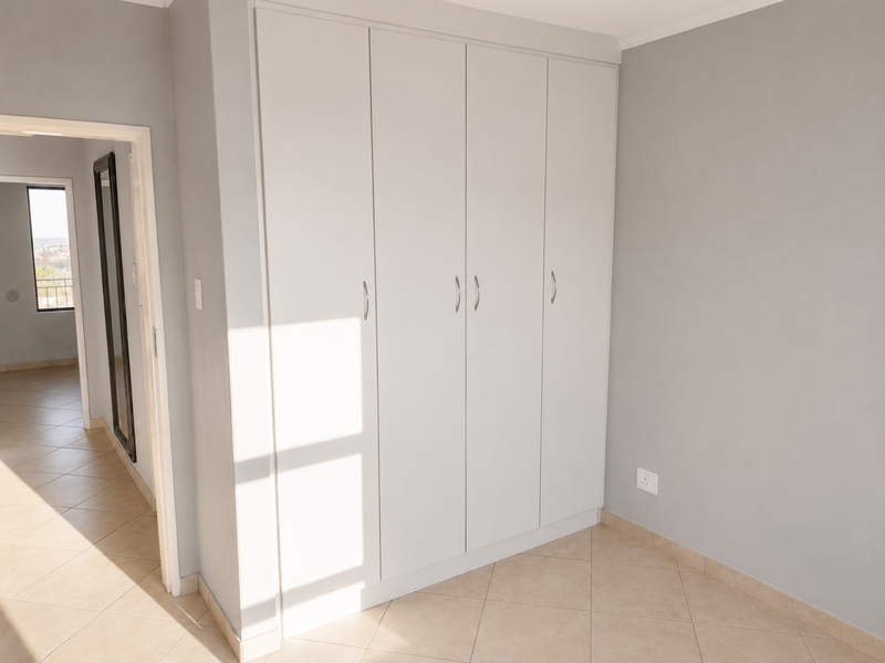 A bright, empty bedroom featuring neutral grey walls, tiled flooring, and ample built-in cupboard storage space.