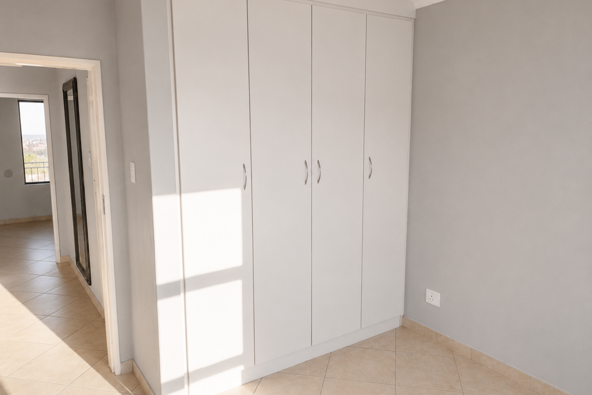 A bright, empty bedroom featuring neutral grey walls, tiled flooring, and ample built-in cupboard storage space.