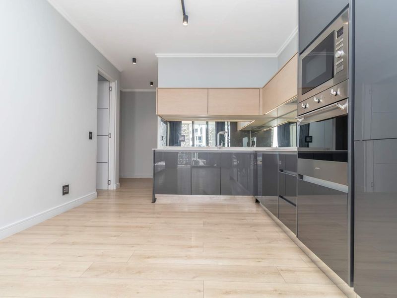 Modern kitchen featuring sleek grey and light wood cabinetry, integrated appliances, mirror splashback, and high-quality laminate flooring in an open-plan layout.