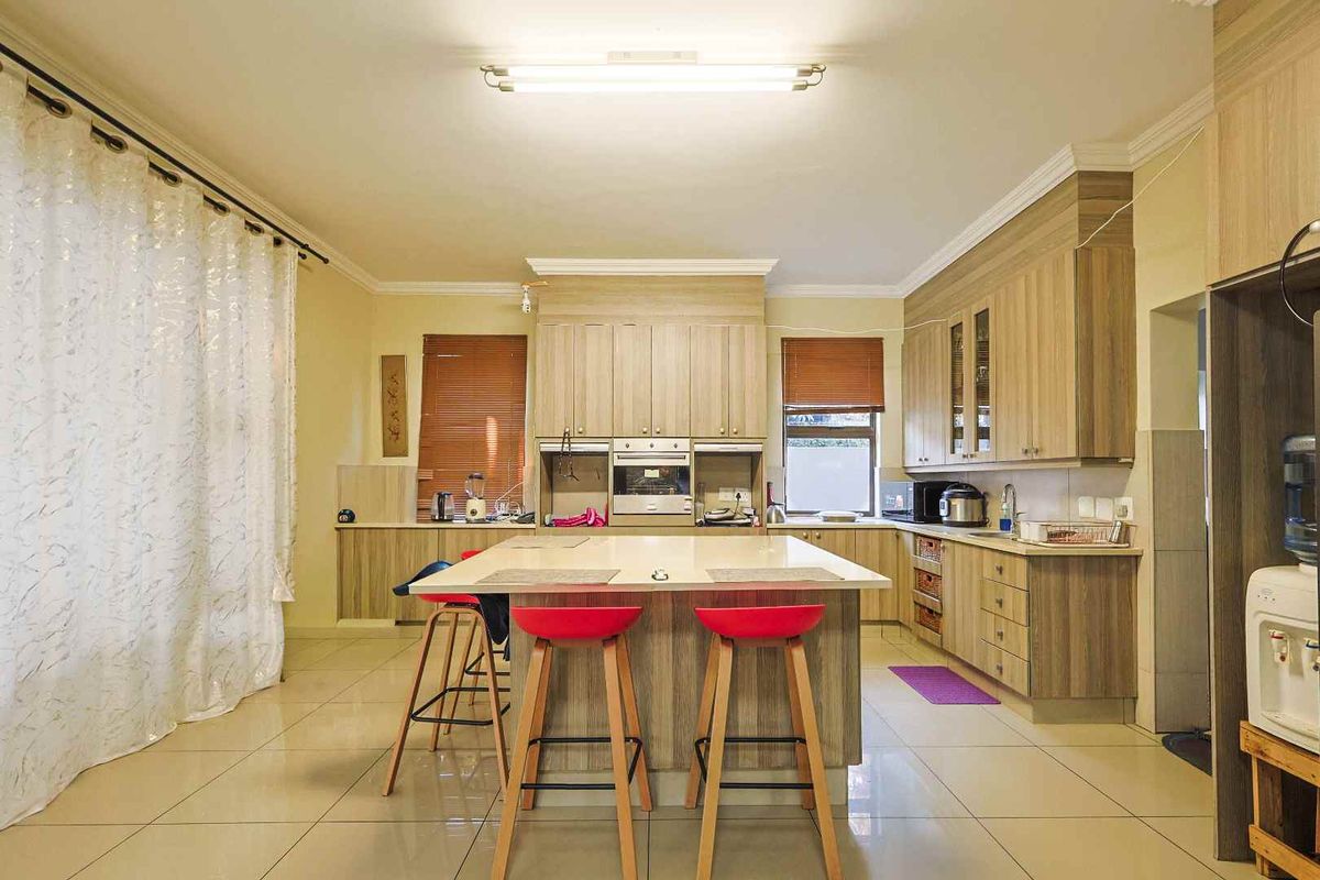 Spacious kitchen featuring wood-finish cabinetry, a central island with stone countertop, built-in oven, and tiled flooring throughout.
