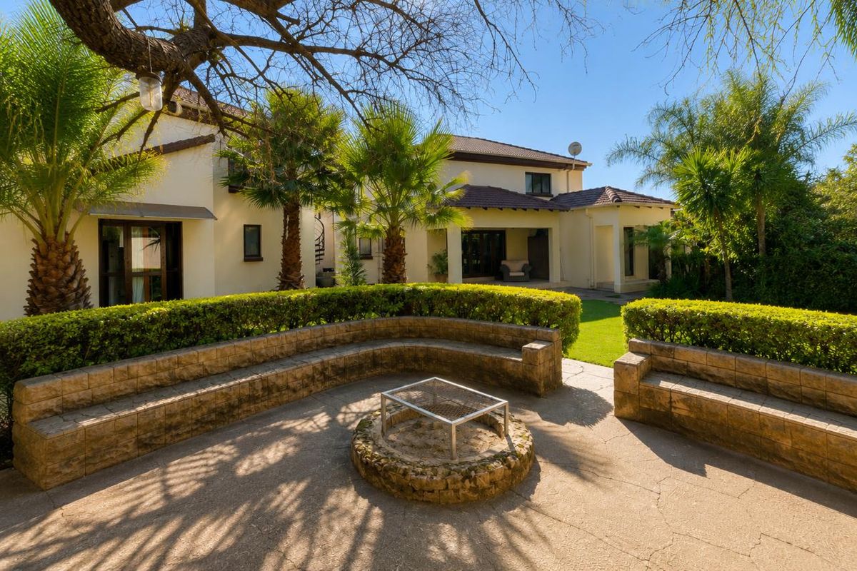A spacious rear garden featuring a paved patio area with a built-in stone fire pit, curved bench seating, and established landscaping.