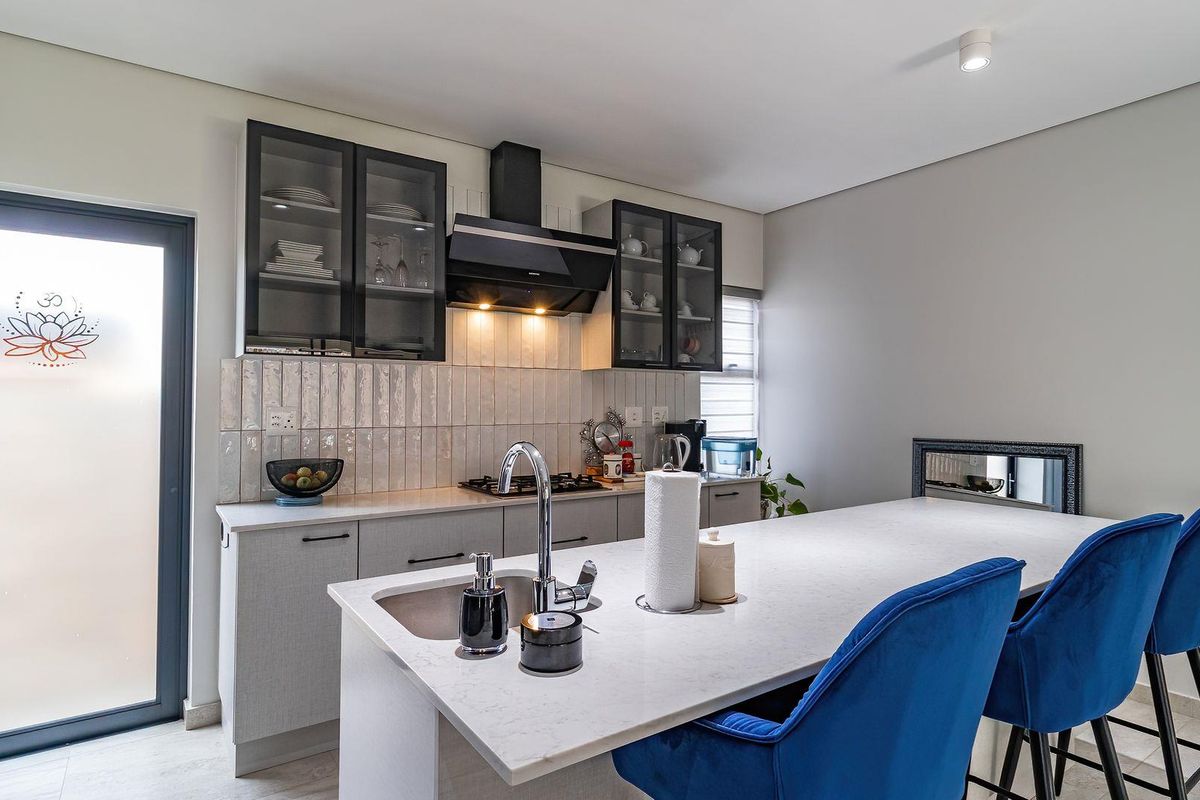 Modern kitchen featuring sleek grey cabinetry, stone countertops, a central island with sink, and a gas hob with a contemporary extractor fan.