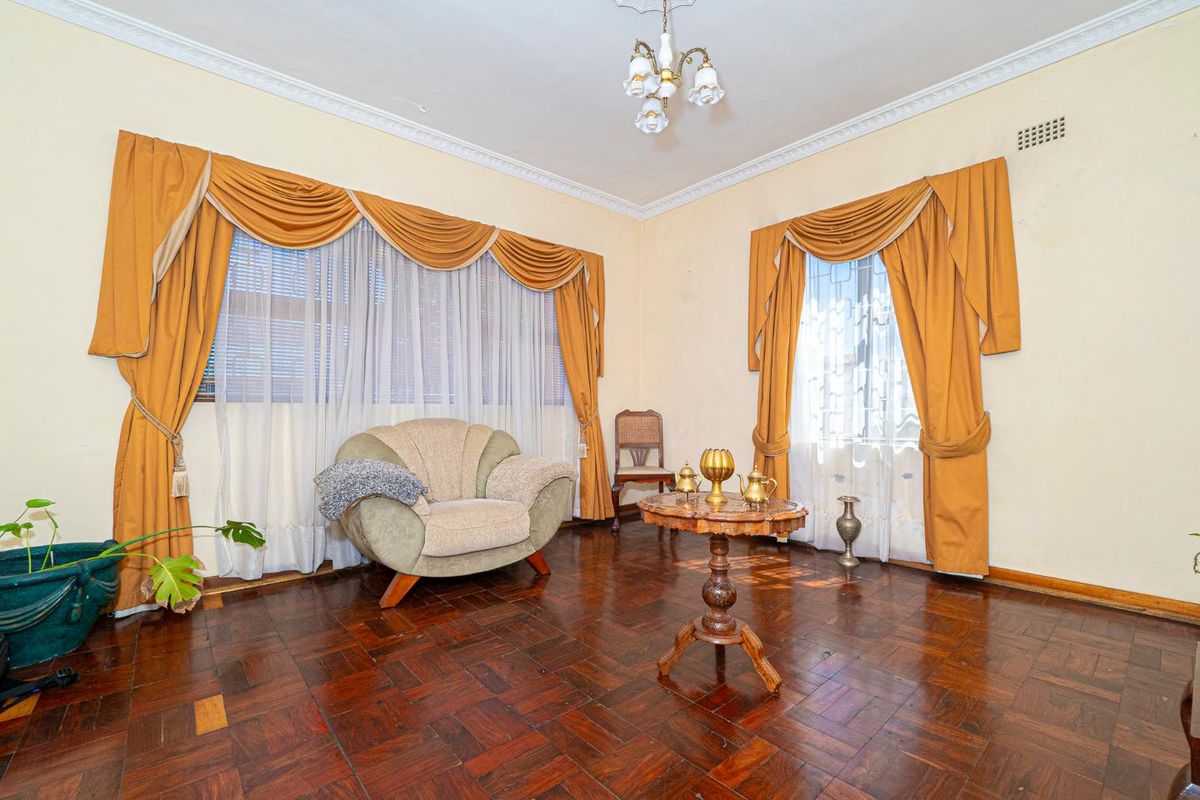 A living room featuring classic parquet flooring, decorative ceiling rose, and ornate cornice detailing, offering a traditional aesthetic with potential for modern updates.